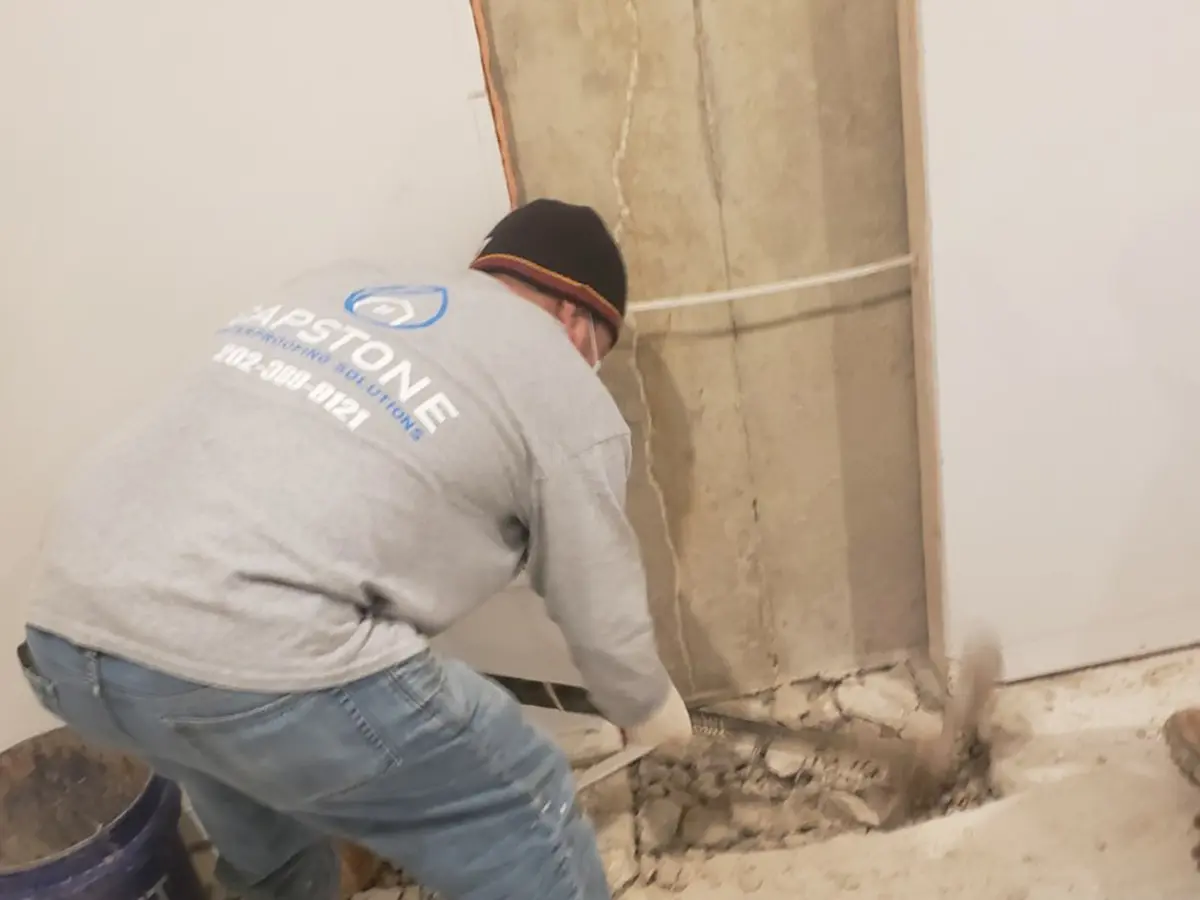 A team member of Capstone using a pickaxe on a basement floor