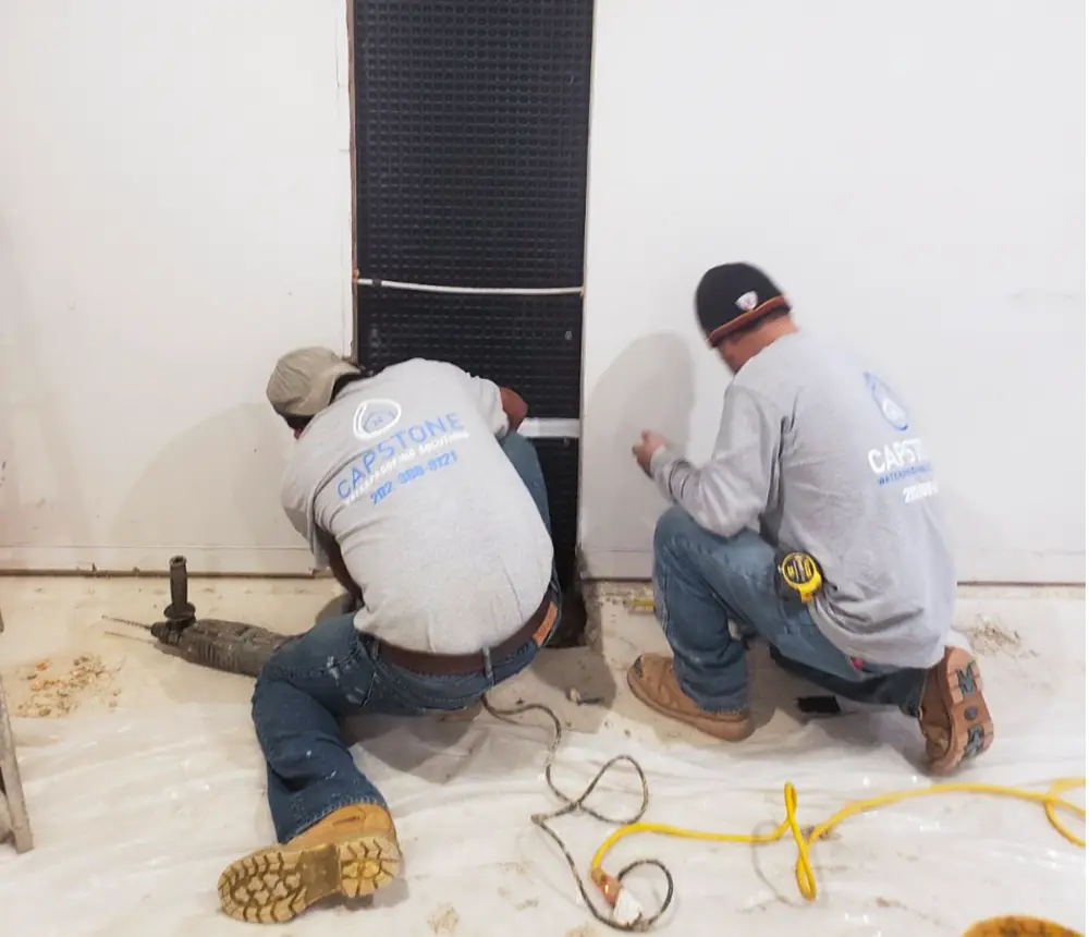 Two Capstone team members working on waterproofing a basement