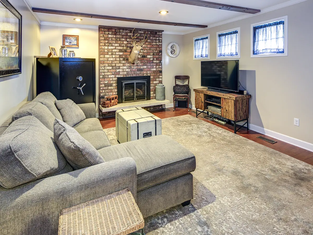 A basemetn with carpet and hardwood flooring, a TV, a fireplace, and a gray couch