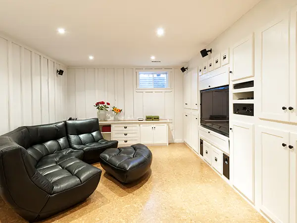 A basement with epoxy flooring, white cabinets, a large black couch, and a TV