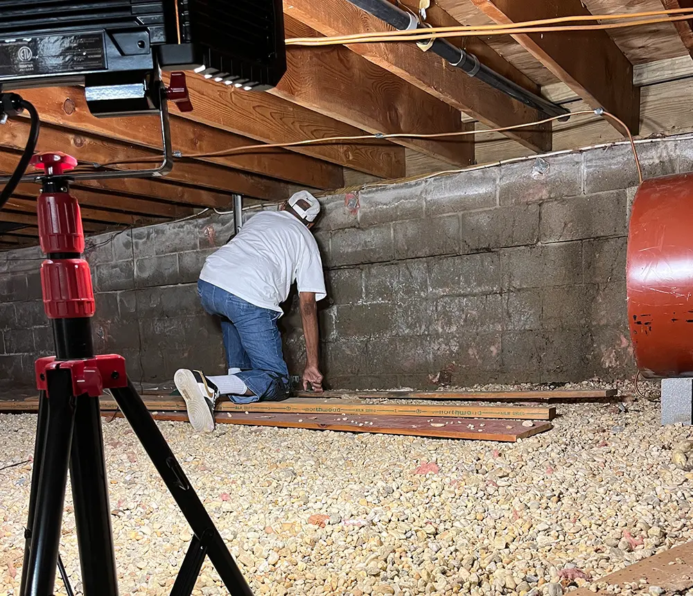 A man underneath a home checking the basement walls