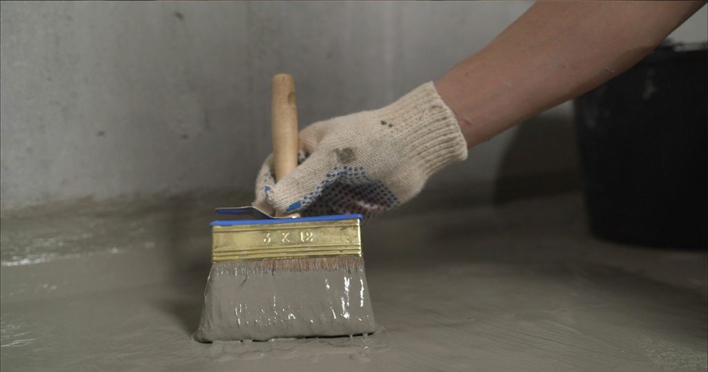 Basement sealing in the form of concrete being applied by brush