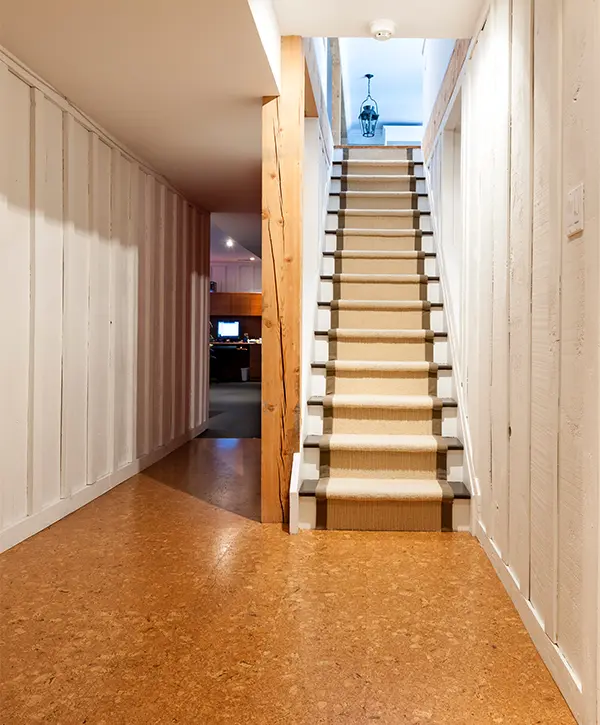 A set of stairs that lead upstairs in a basement with cork flooring