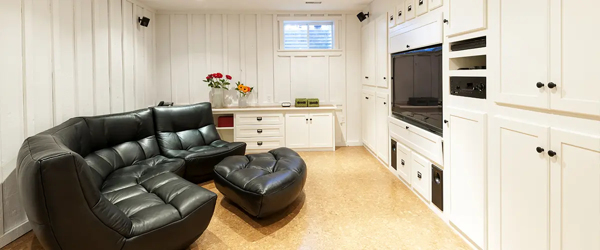 A large living space in a basement with a leather couch and a TV
