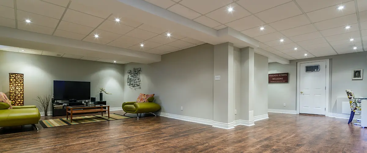 Spacious finished basement in Hyattsville, with recessed lighting, wood flooring, green armchairs, and a modern entertainment setup against a light gray wall.